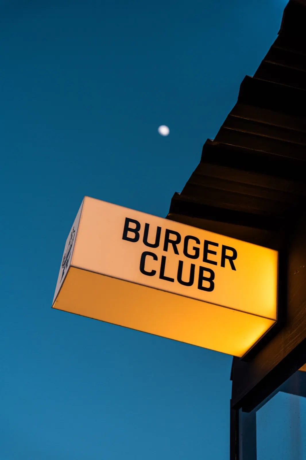 Burger Club illuminated sign at dusk with the moon in the background