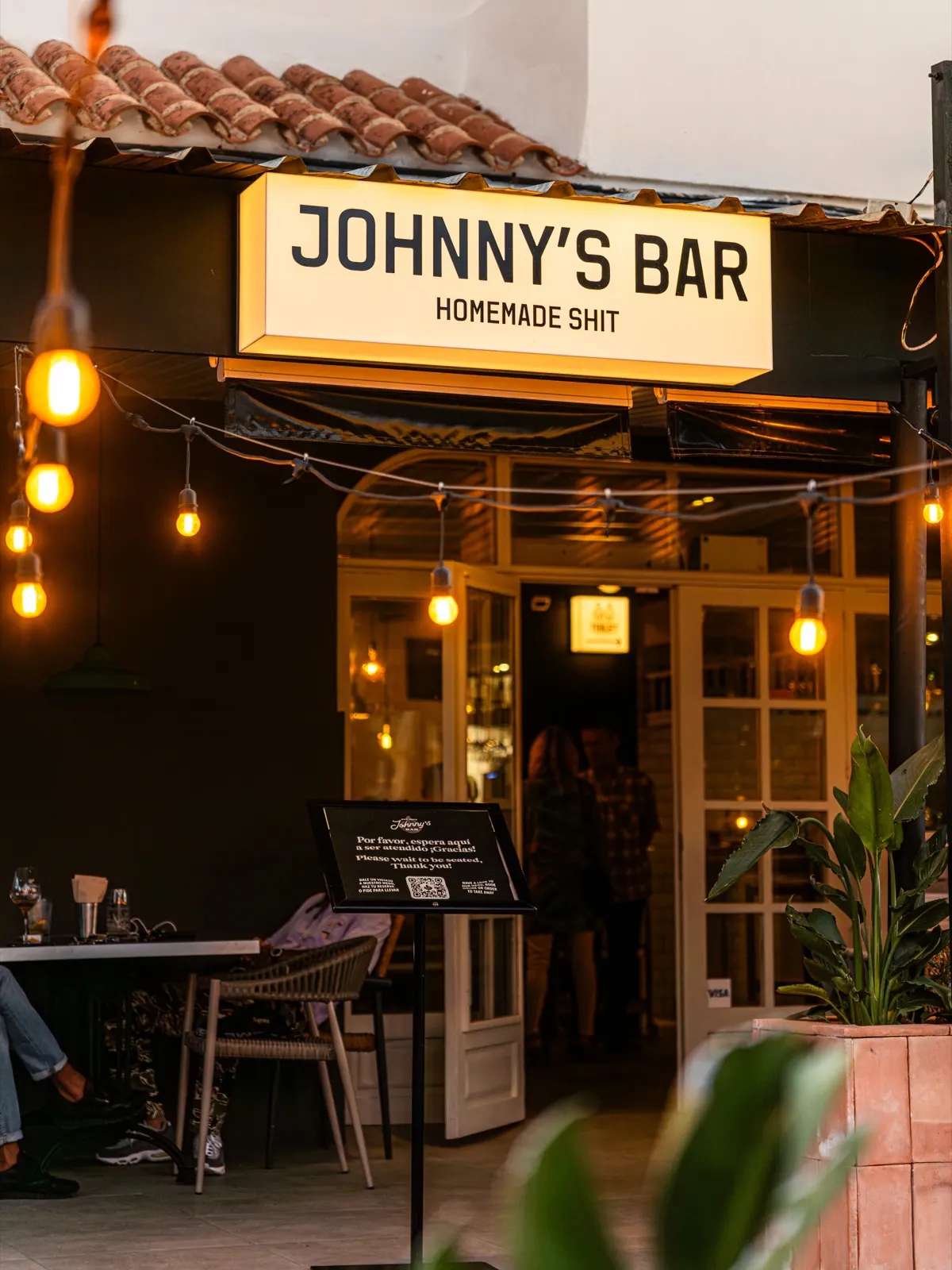 Johnny's Bar entrance with Homemade Shit sign and lights at dusk