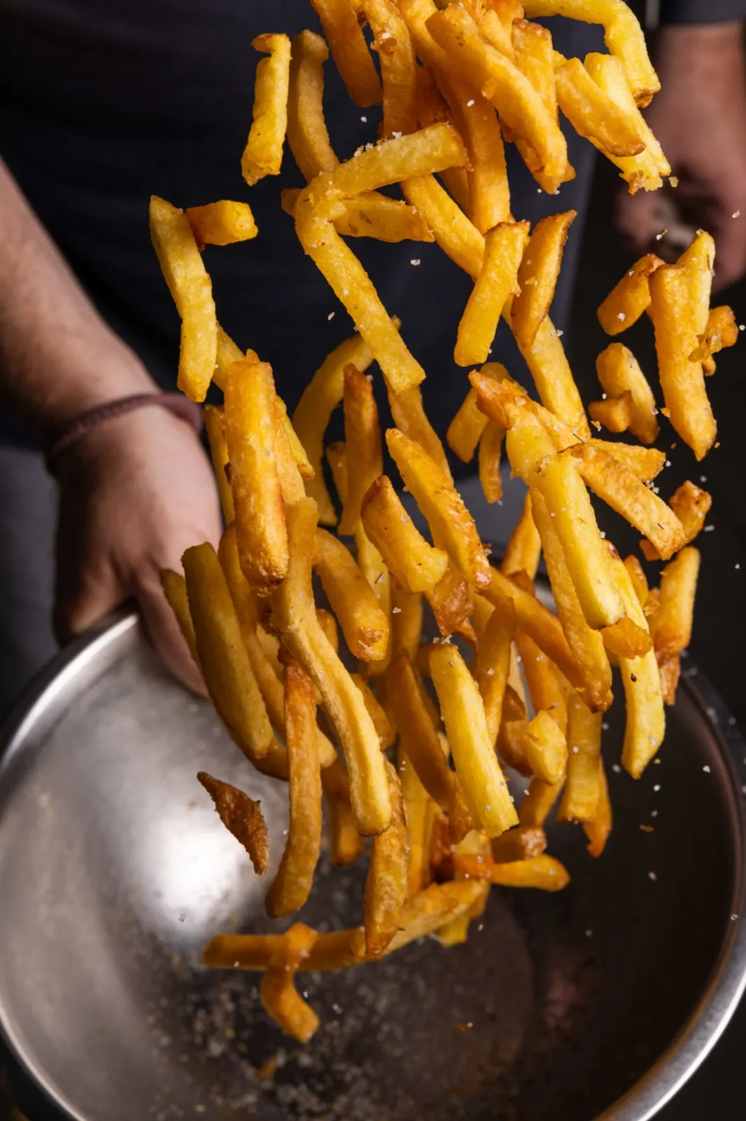 Homemade fries tossed in a pan with salt